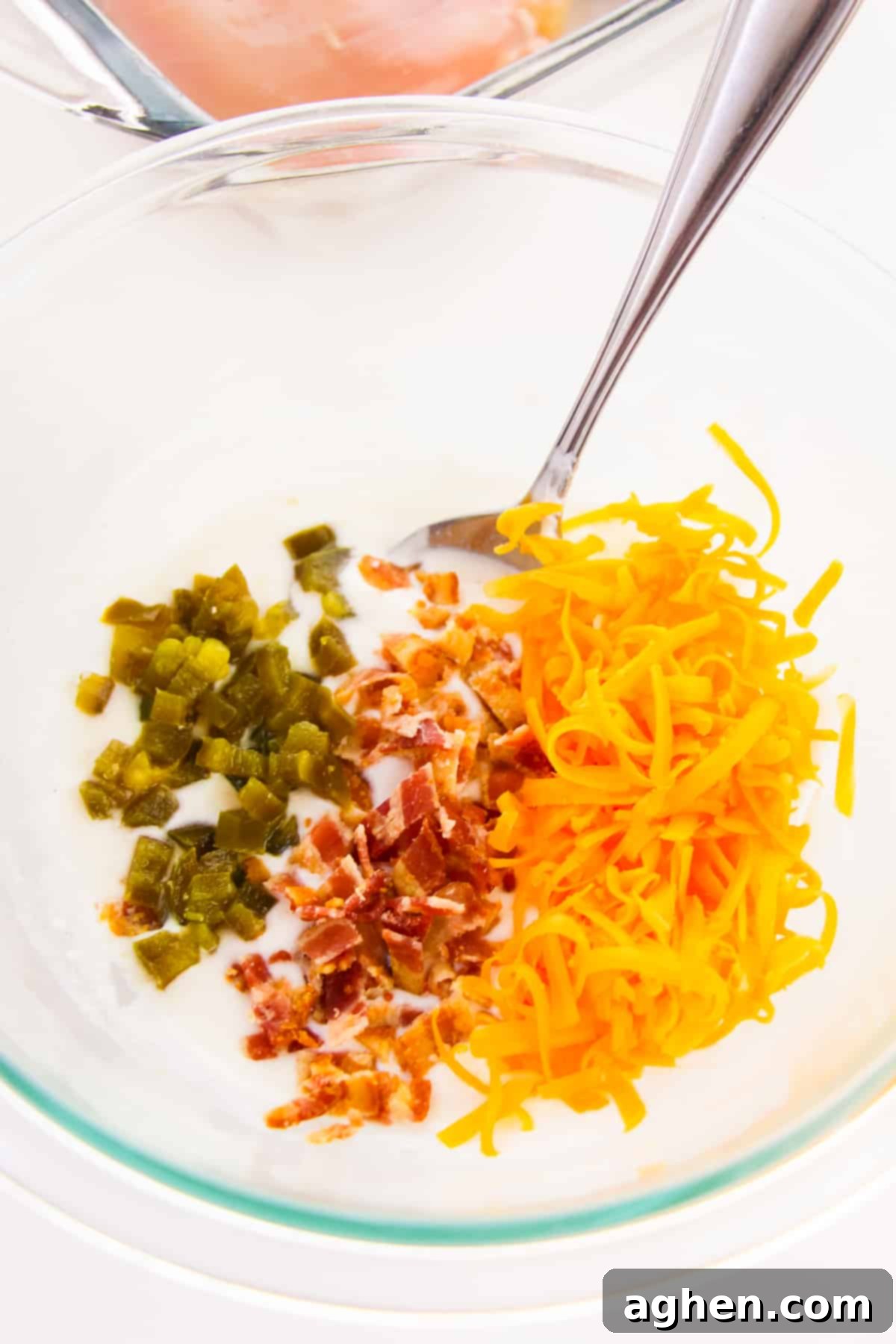 Mixing bowl with sour cream, mayonnaise, diced jalapeños, chopped bacon, and shredded cheddar cheese, ready to be combined for the topping.