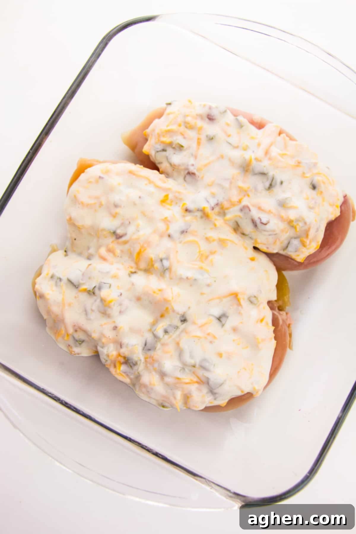 Chicken breasts topped with a creamy jalapeño mixture in a glass baking dish, ready for baking.