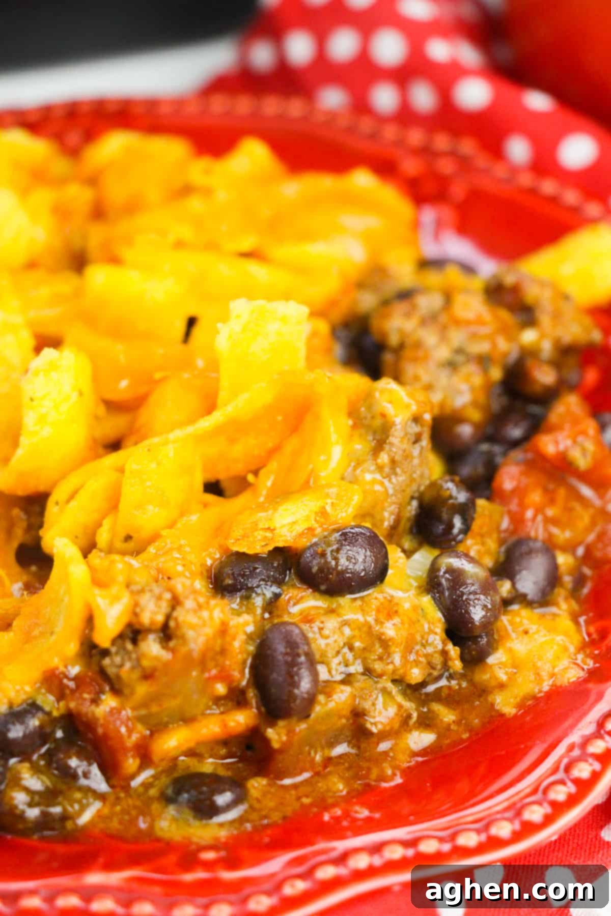 A serving of Frito pie on a vibrant red plate, showcasing the layers of seasoned meat, melted cheese, and golden Fritos corn chips, ready to be enjoyed.