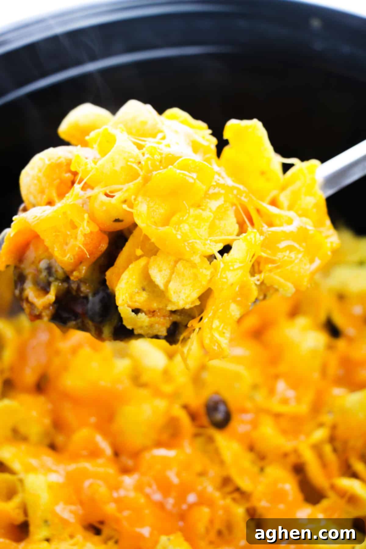A large serving spoon is gently removing a generous spoonful of hot, cheesy Frito Casserole from the crockpot, highlighting the hearty layers of meat, beans, and melted cheese, ready for serving.