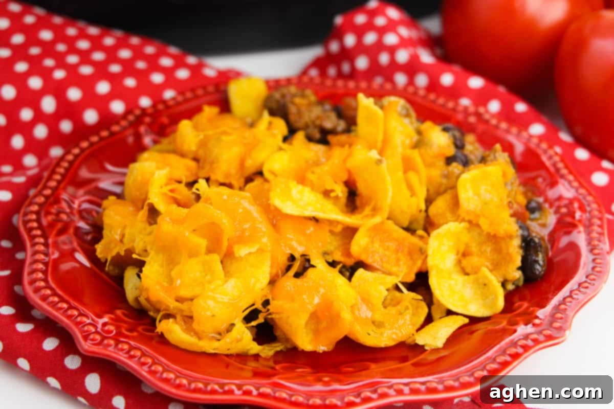A perfectly portioned Crockpot Frito Casserole on a red plate, accompanied by a festive red napkin and fresh tomatoes in the soft-focused background, emphasizing its homemade appeal.