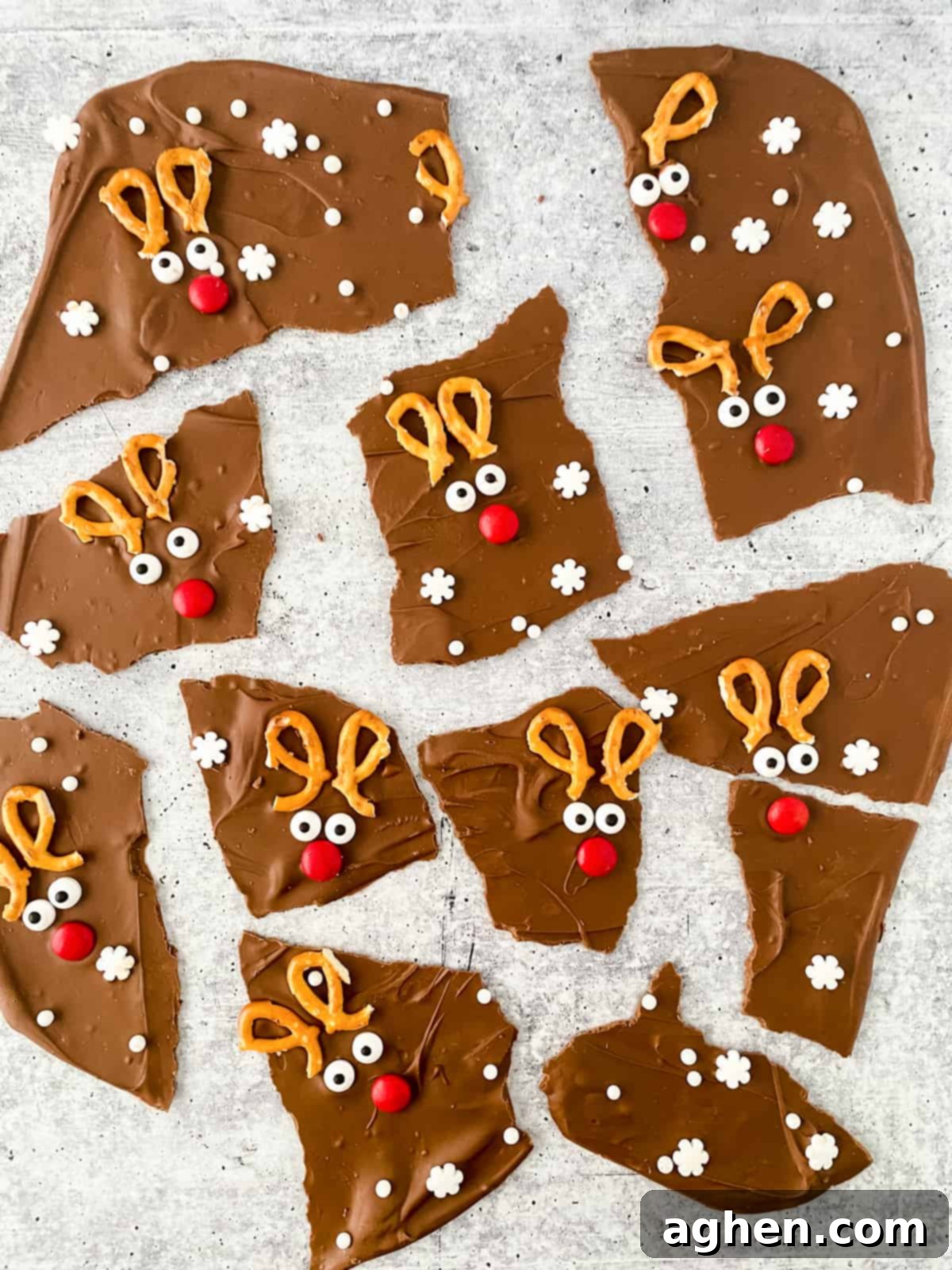 Chocolate reindeer bark broken into irregularly shaped pieces, each decorated with broken pretzels, candy eyes, and a red M&M to look like Rudolph the red-nosed reindeer, laid out on parchment paper