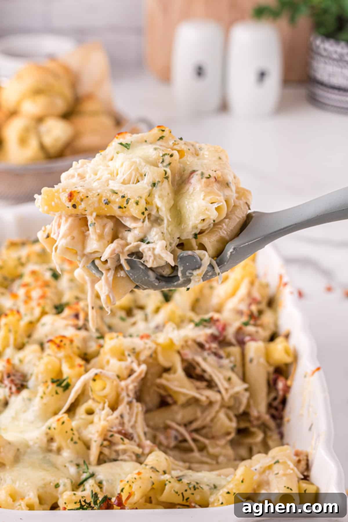 Large grey serving spoon scooping up a large serving of creamy chicken alfredo casserole with bacon, cheese, and parsley
