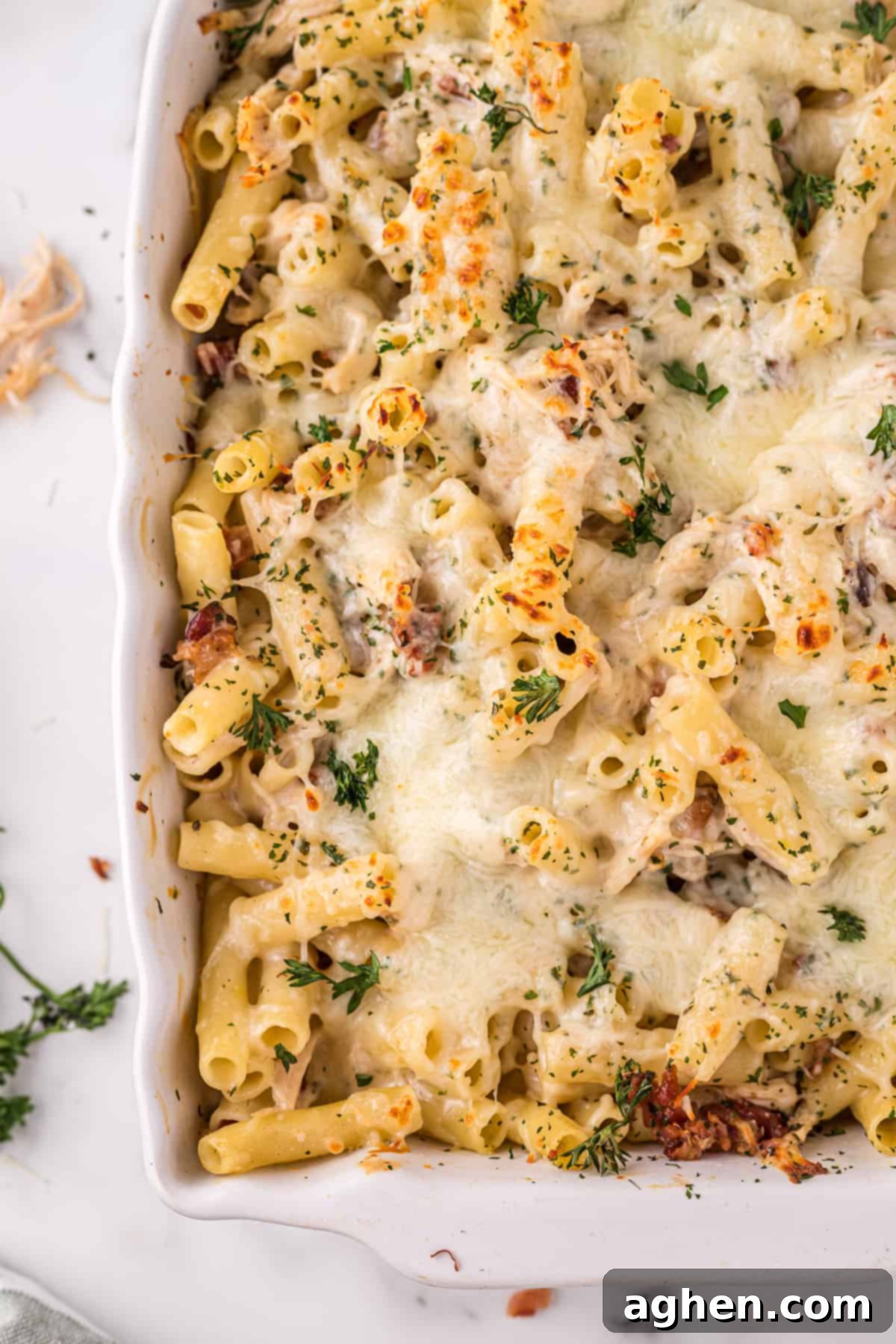 Corner of baking dish with a cheesy chicken bacon alfredo pasta bake garnished with parsley