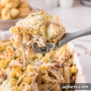 Large grey serving spoon scooping up a large serving of creamy chicken alfredo casserole with bacon, cheese, and parsley