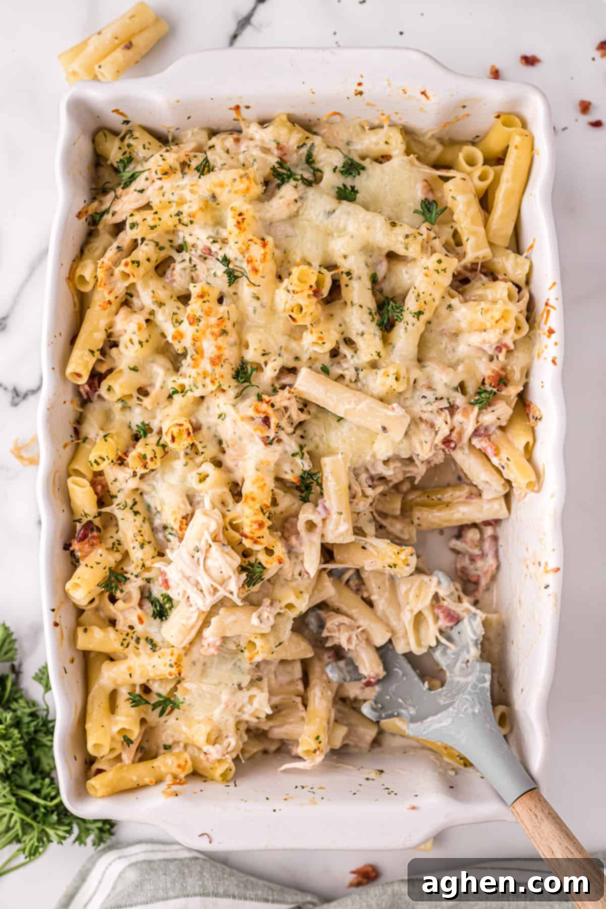 Chicken Bacon Alfredo Pasta Bake in a 9 x 13 casserole dish with a missing portion and serving spoon set inside