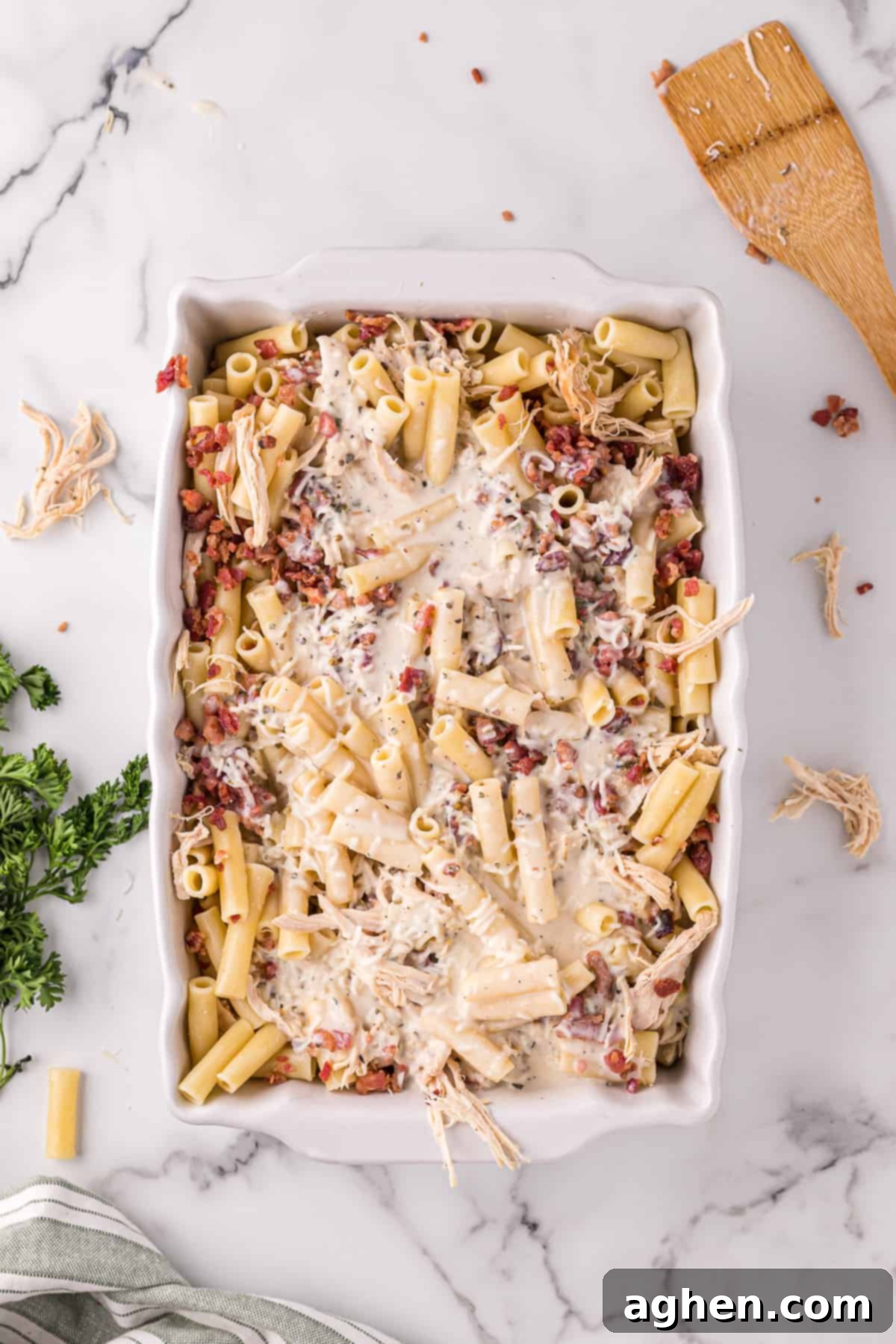 Casserole dish with ziti, crumbled bacon, shredded cooked chicken, and alfredo sauce poured on the top