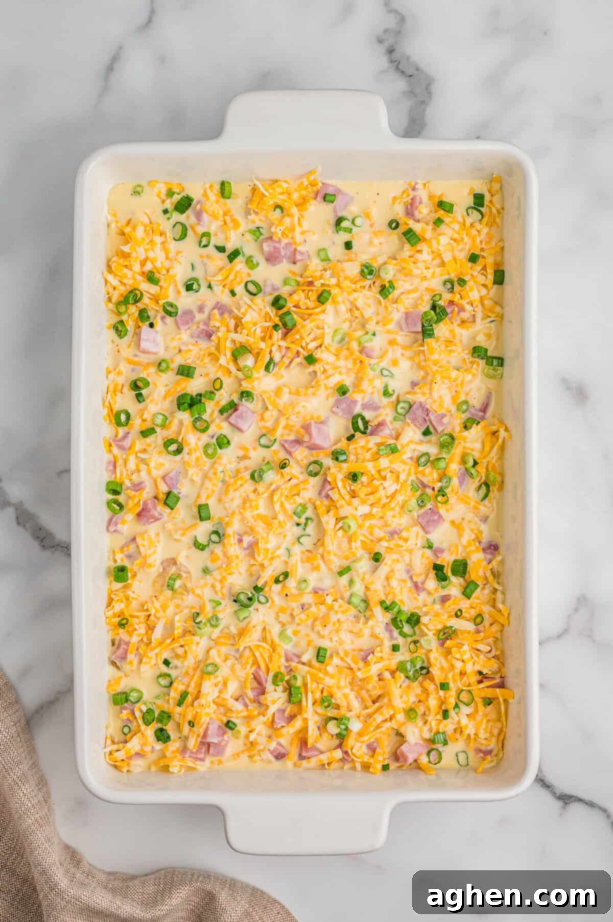 Breakfast casserole ingredients in casserole dish with egg mixture poured over them.