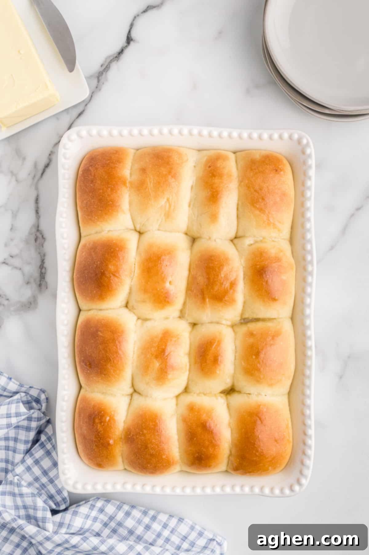 Golden brown potato dinner rolls in baking dish with butter and plates next to them