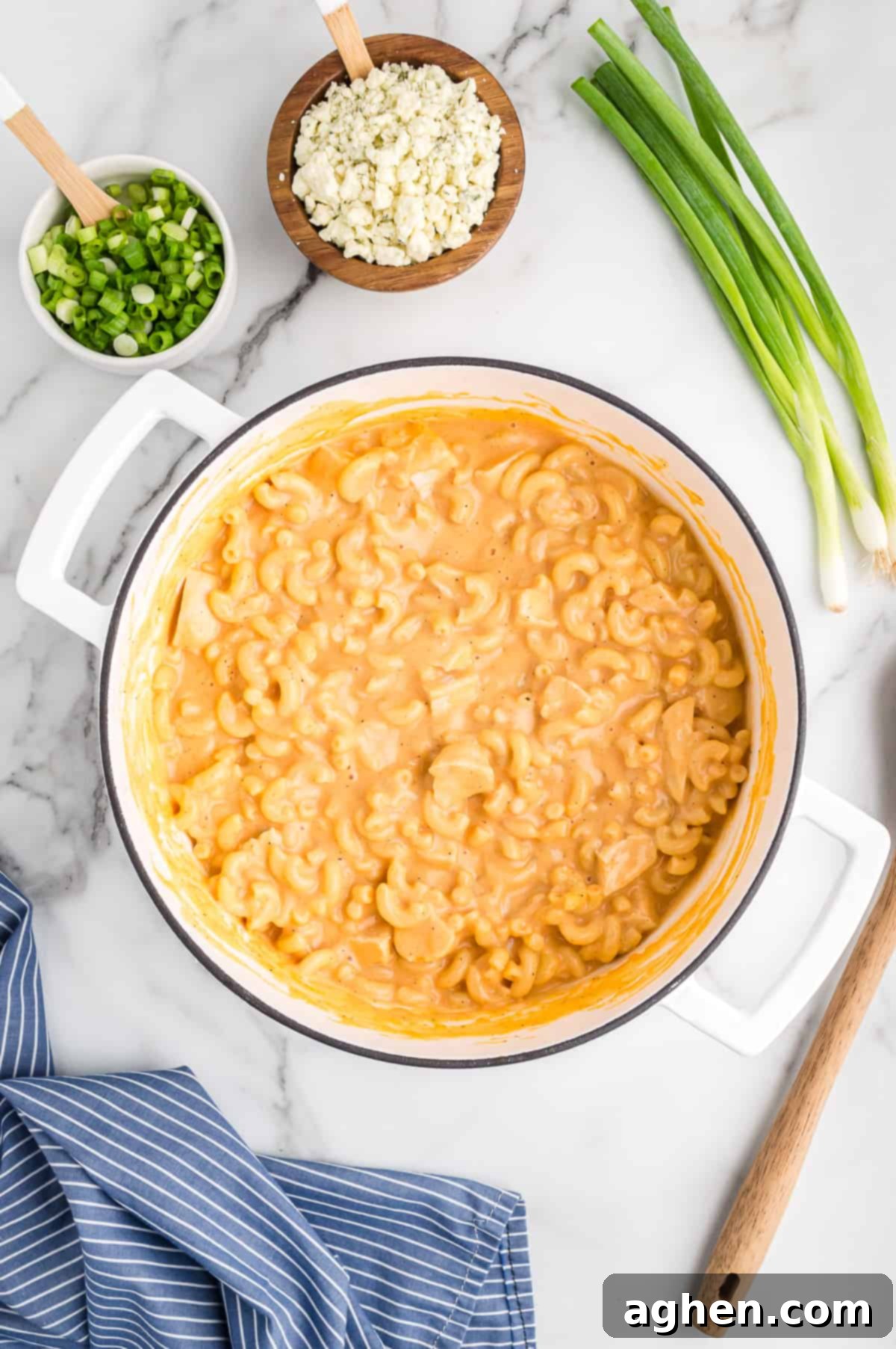 large white pot of buffalo mac and cheese with chicken. Green onions and blue cheese are next to the pot
