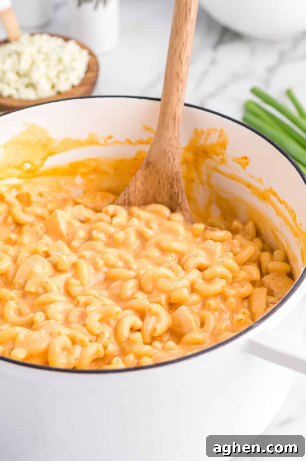 Large white pot of buffalo chicken mac and cheese with blue cheese crumbles and green onions in background