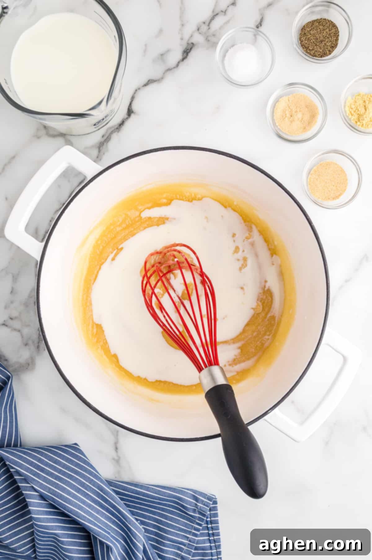 Milk being whisked into roux in large white pot
