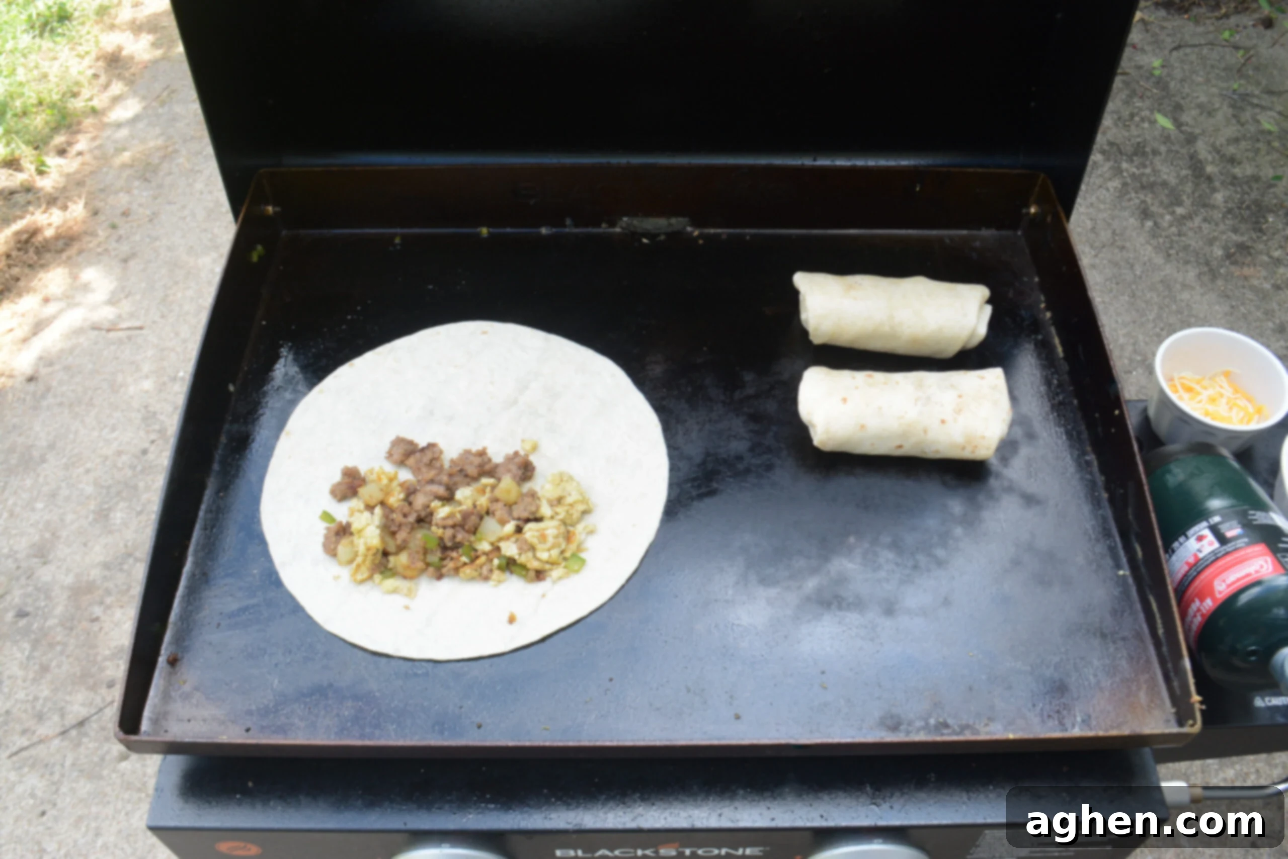 An open tortilla with filling is shown on the Blackstone. Two rolled burritos sit next to it. 