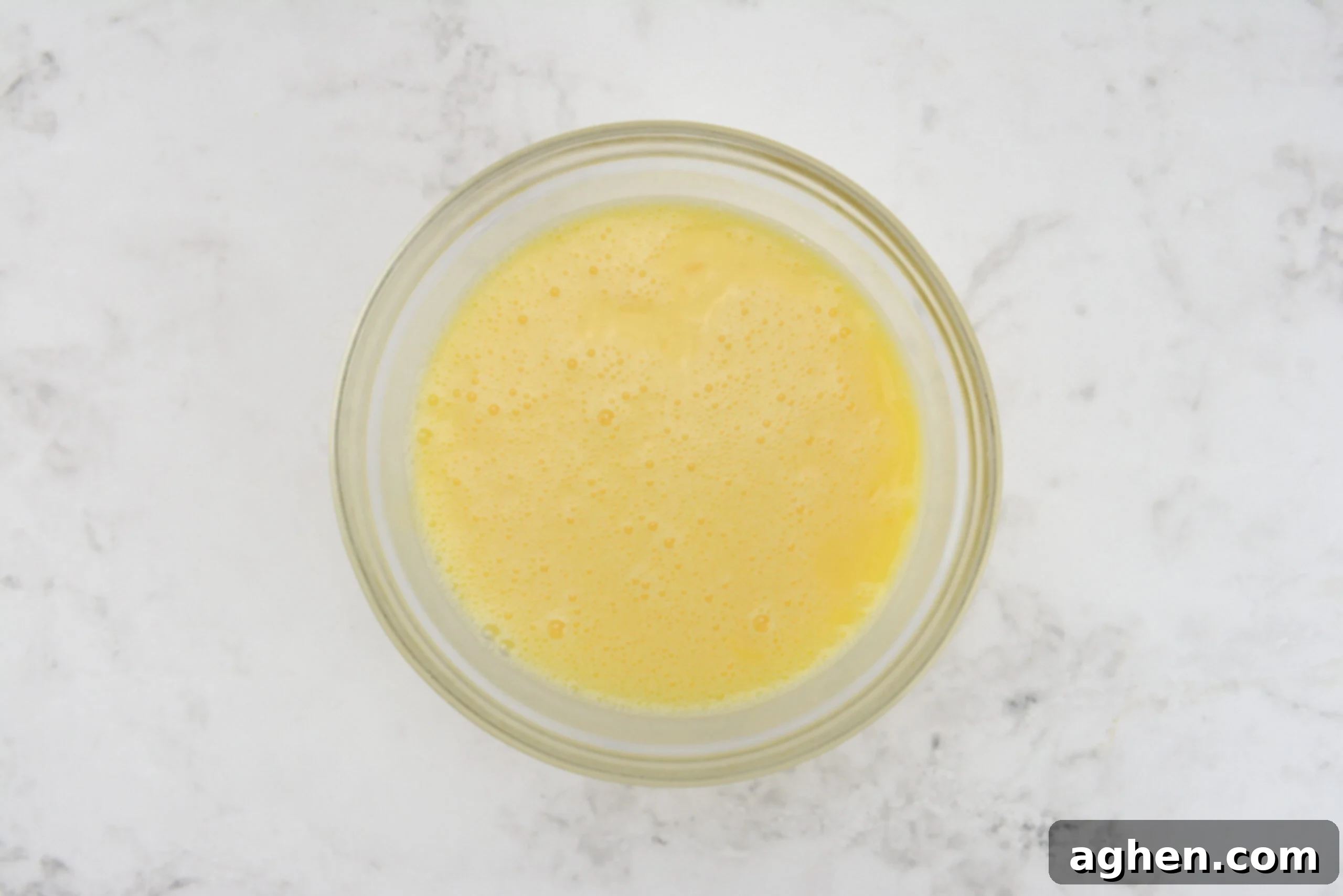 A large clear mixing bowl is filled with whisked eggs