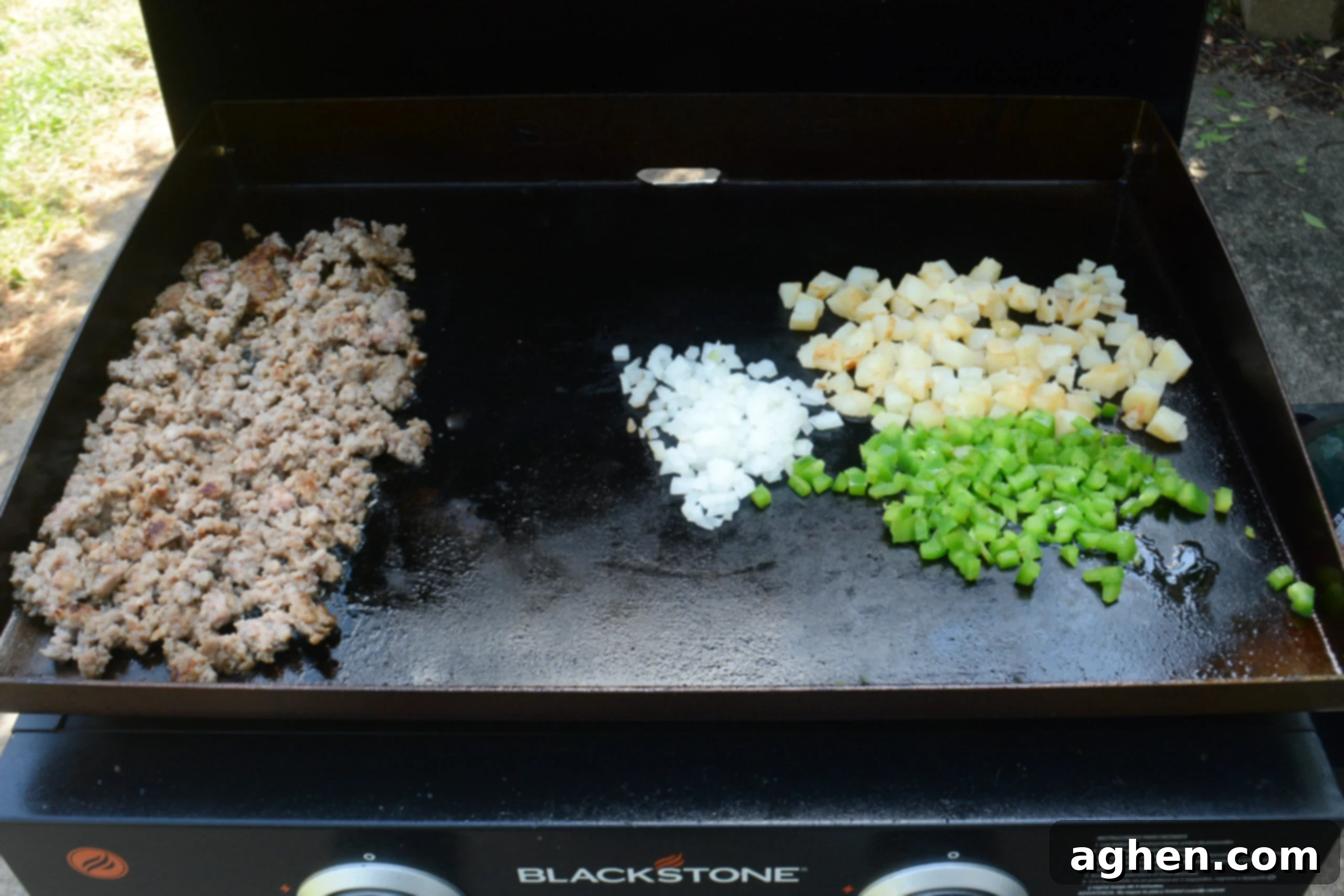 The cooked sausage is pushed to one side while the potatoes, onion, and bell pepper continue cooking on the right side. 