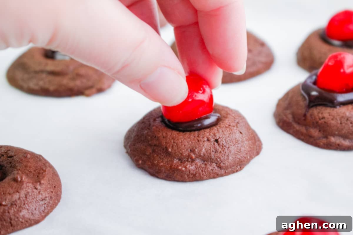 hand placing stemless maraschino cherry on top of chocolate thumbprint cookie
