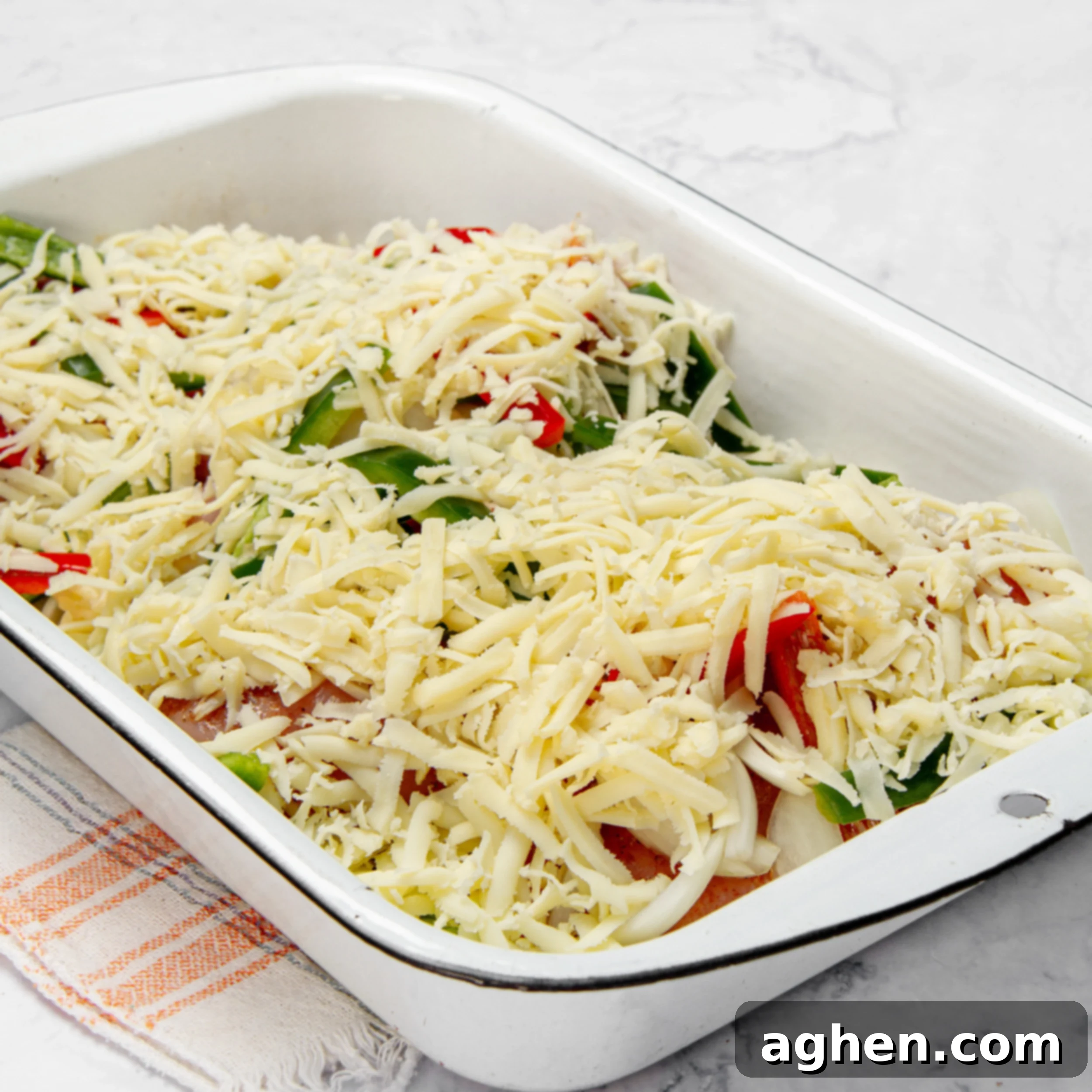Chicken breasts topped with a colorful array of vegetables and cheese in a casserole dish, prior to baking.