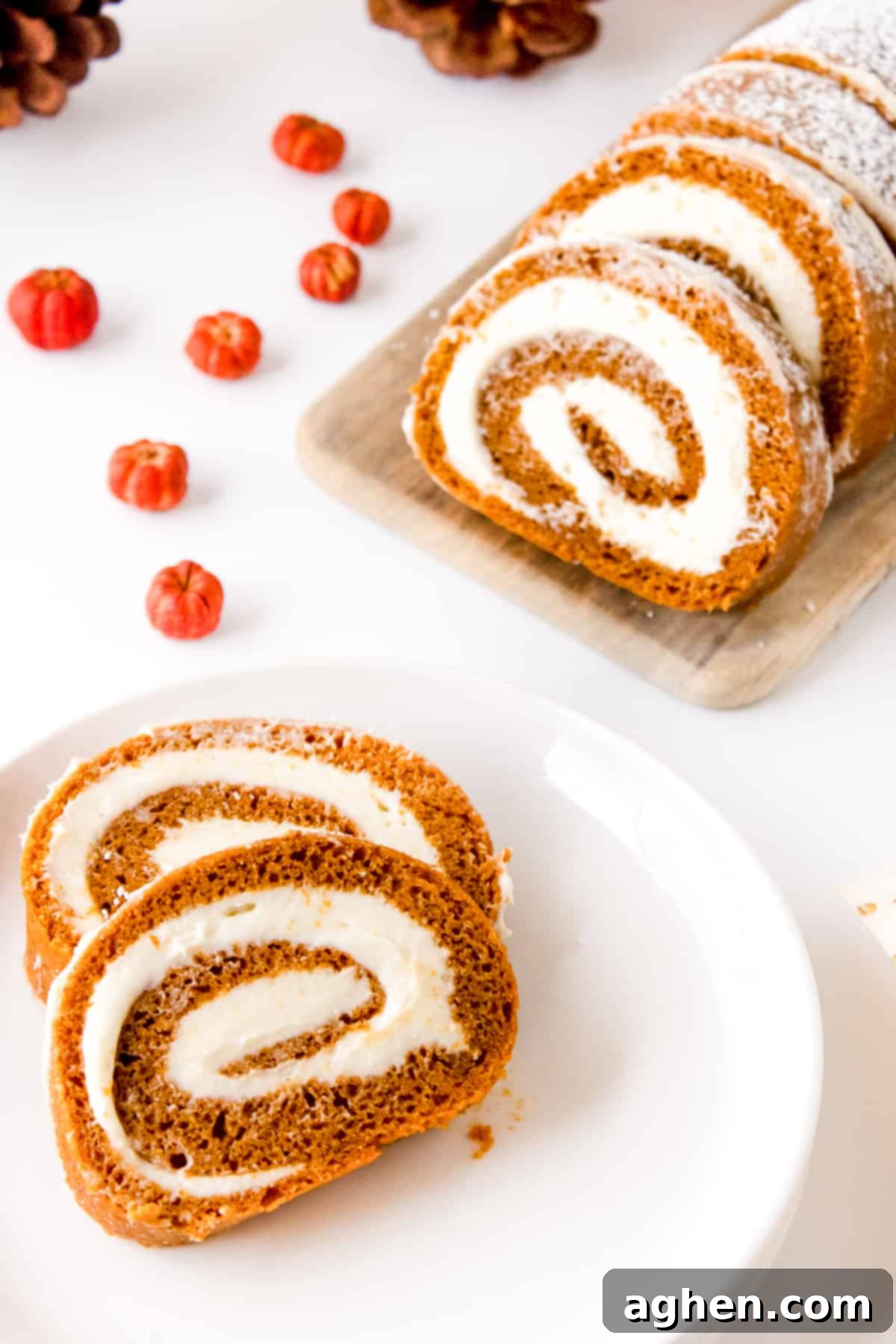 Autumn Pumpkin Cream Cheese Roll 12 Perfectly sliced pumpkin roll cake on a white plate with additional slices on a light wood board, showcasing the creamy filling swirl.