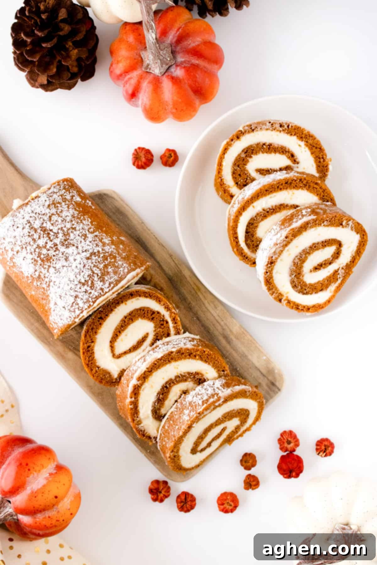 Autumn Pumpkin Cream Cheese Roll 3 Slices of Pumpkin Roll Cake with Cream Cheese Filling on a white plate and wooden cutting board, decorated with small pumpkins for a festive fall look.