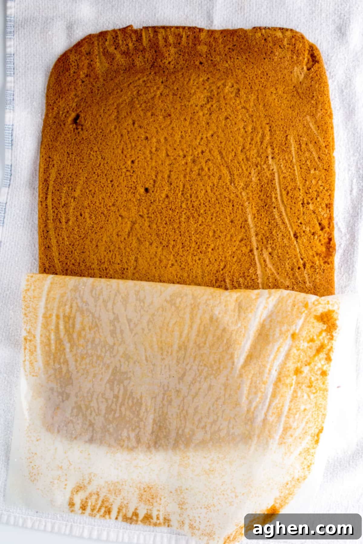 Autumn Pumpkin Cream Cheese Roll 7 Parchment paper being carefully peeled off a warm, freshly baked pumpkin cake.