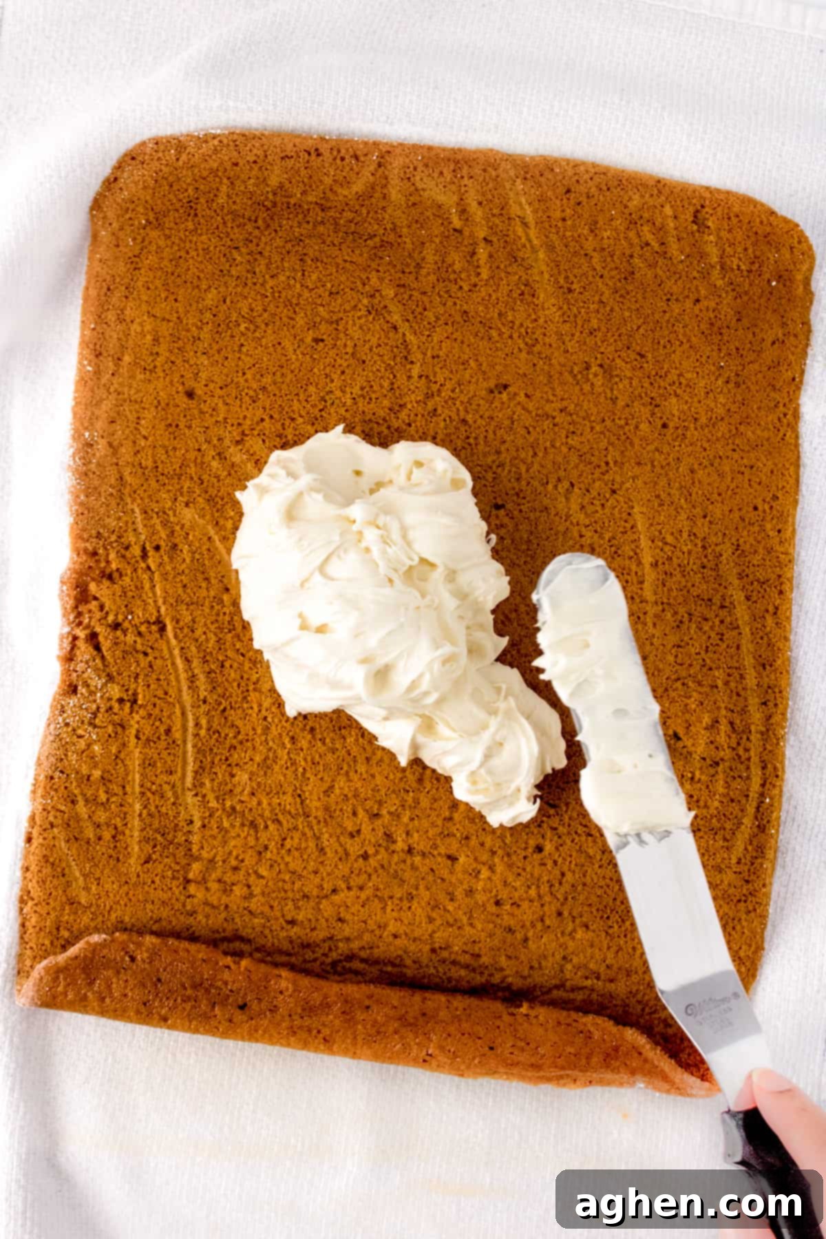 Autumn Pumpkin Cream Cheese Roll 10 Cream cheese frosting being expertly spread with an offset spatula onto an unrolled pumpkin cake, ready for re-rolling.