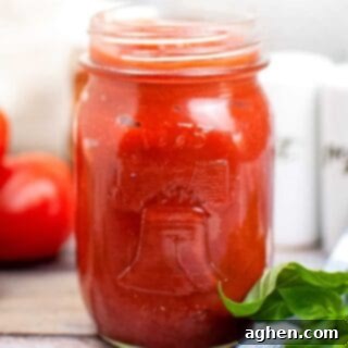 Homemade pizza sauce in a mason jar on a wooden table, surrounded by fresh ingredients like tomatoes, garlic, and basil.