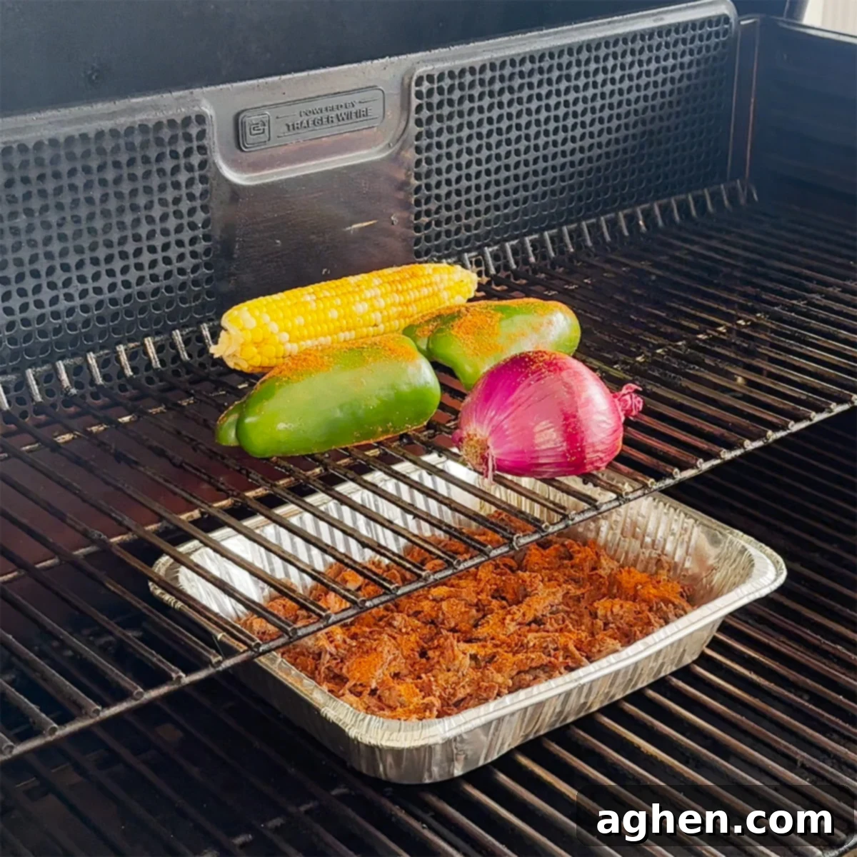 Pulled beef, halved green peppers, and onions seasoned with taco spice, smoking on the grates of a Traeger grill.