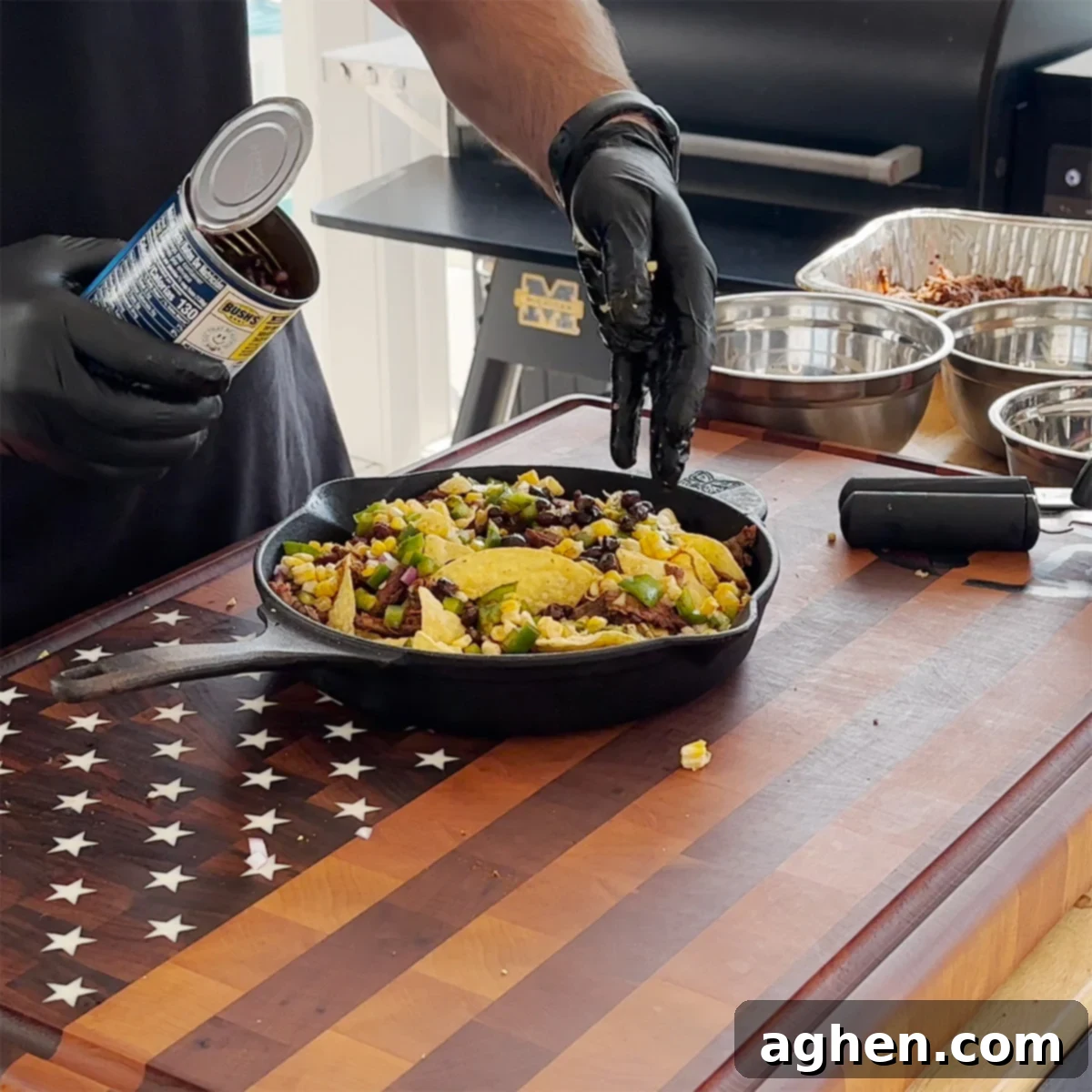 A cast iron skillet layered with tortilla chips and various toppings like pulled beef, peppers, onions, and beans.