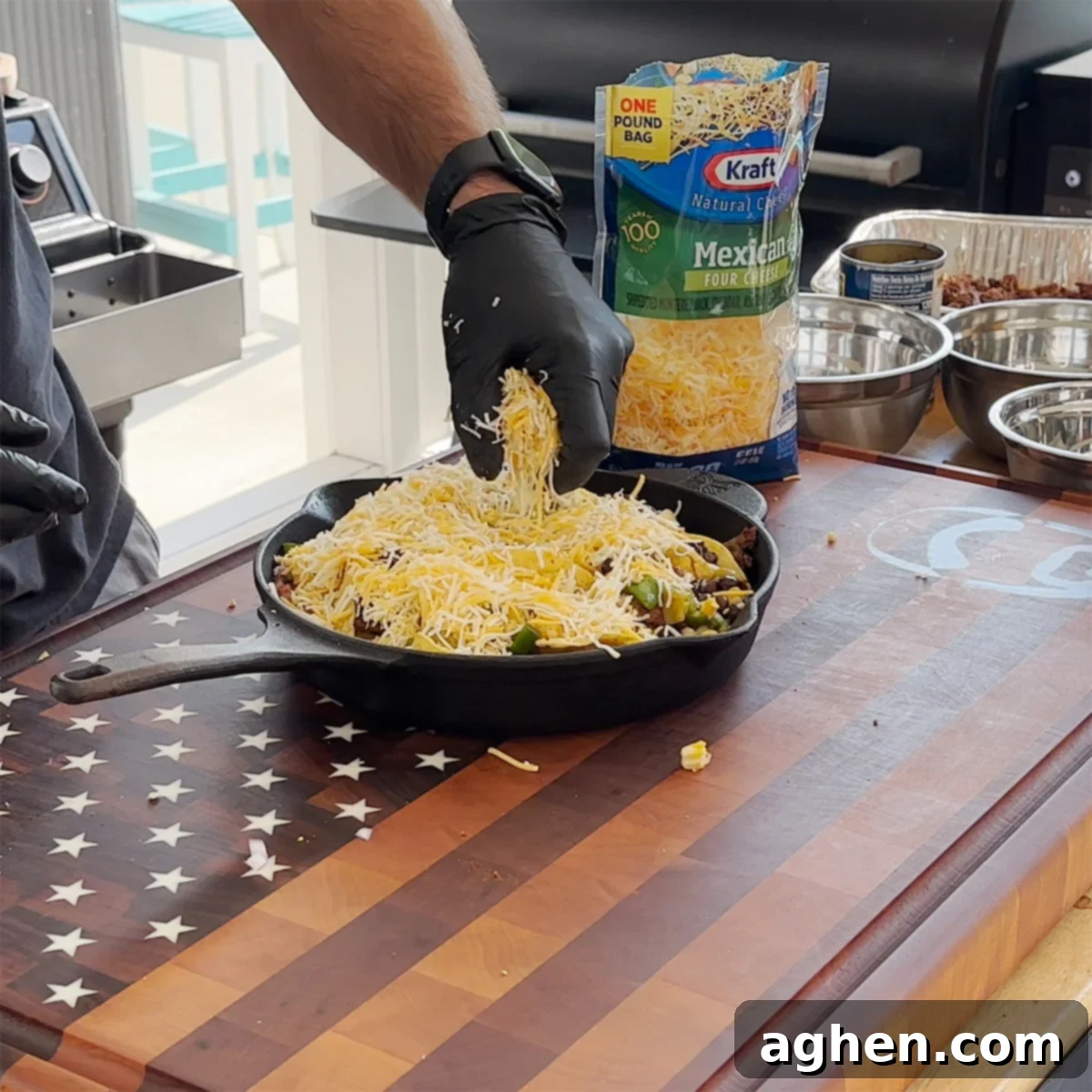 A cast iron skillet of layered nachos generously covered with shredded Mexican cheese blend, ready for the grill.