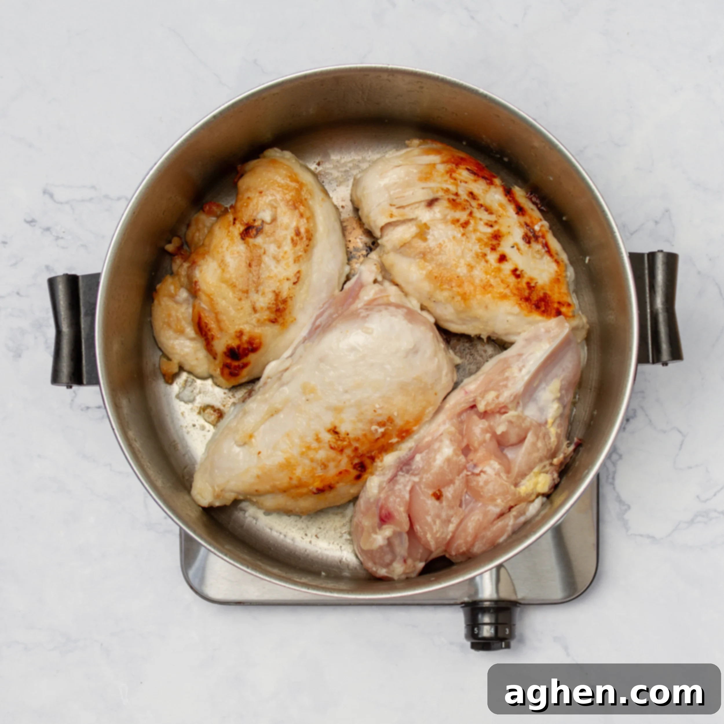 Seasoned chicken breasts searing in a pot. 