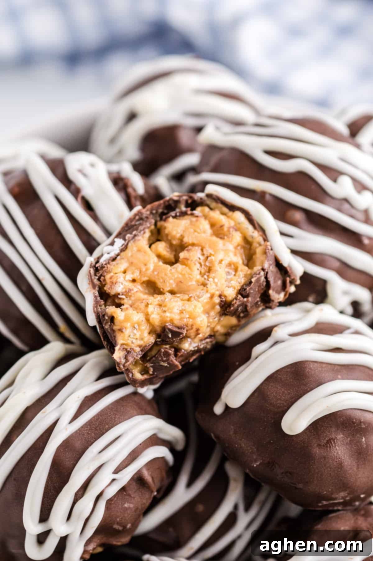 No-Bake Peanut Butter Crunch Bites 2 Peanut Butter Balls with Rice Krispies piled high in a bowl. The top one is cut in half to show creamy peanut butter filling with crunchy texture.