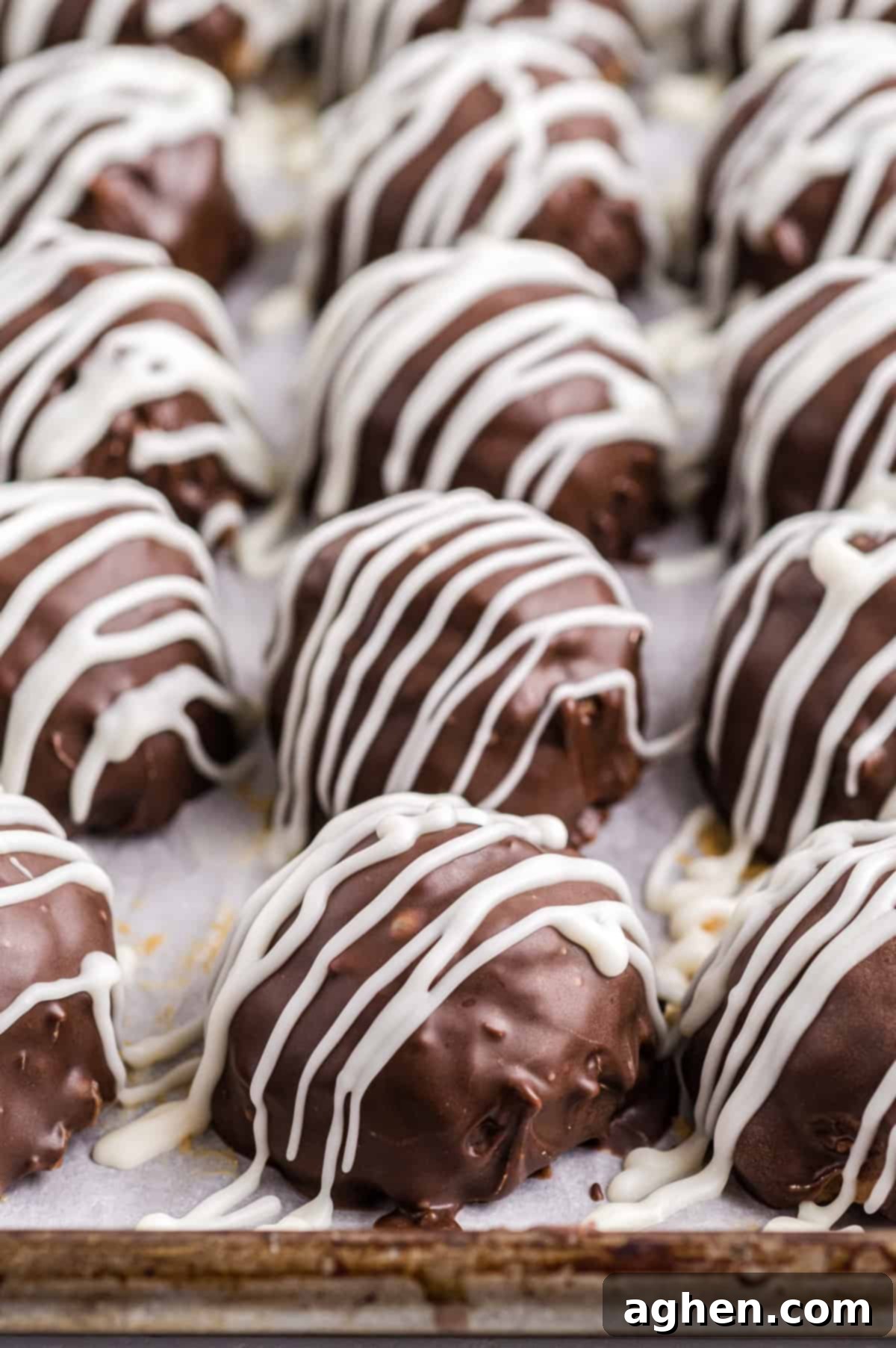 No-Bake Peanut Butter Crunch Bites 3 Chocolate Rice Krispies Peanut Butter Balls drizzled with white chocolate on a lined baking sheet.