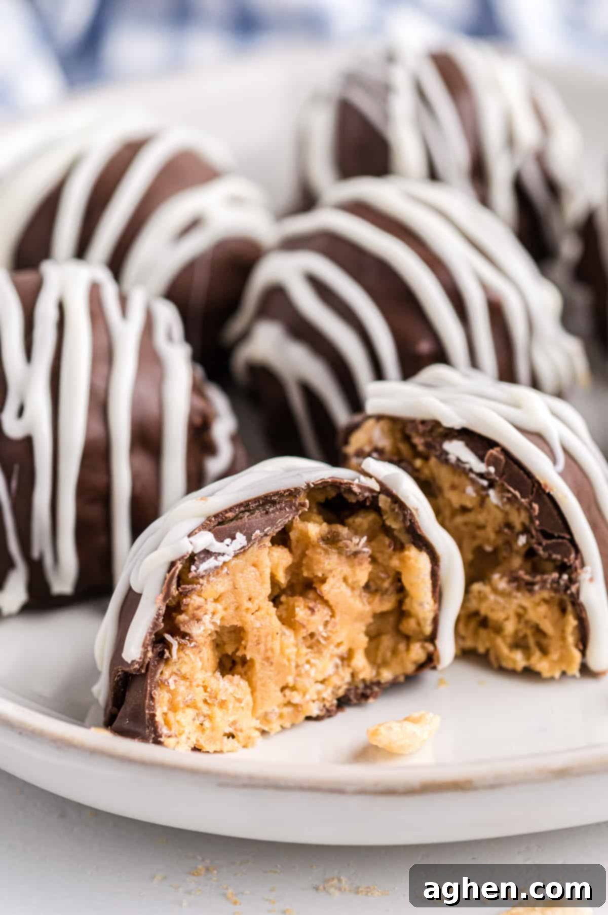 No-Bake Peanut Butter Crunch Bites 9 Chocolate Rice Krispie Balls on a white plate with one cut in half to show creamy peanut butter and crunchy rice cereal inside.