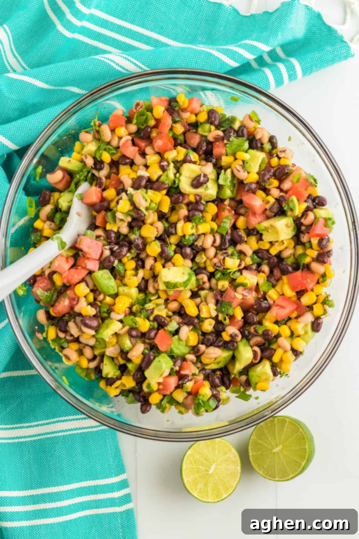 Finished Cowboy Caviar in a large glass bowl with a serving spoon, showcasing the colorful mix of beans, corn, avocado, and vegetables coated in dressing.