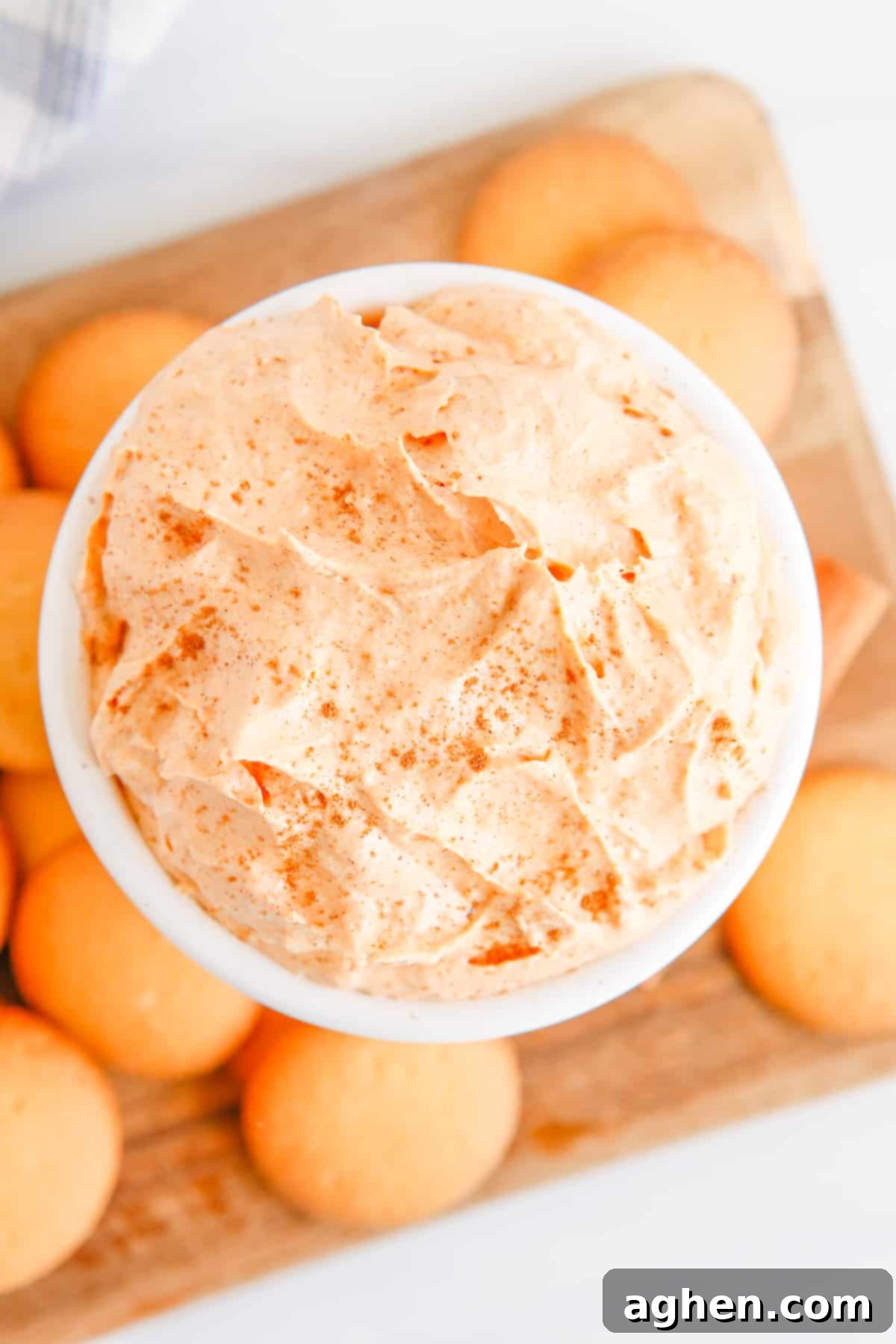 Overhead view of fluffy pumpkin dip in a white bowl surrounded by vanilla wafers for serving.