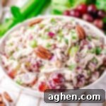 Chicken grape and pecan salad in a white bowl with fresh red grapes, celery, and lettuce behind it