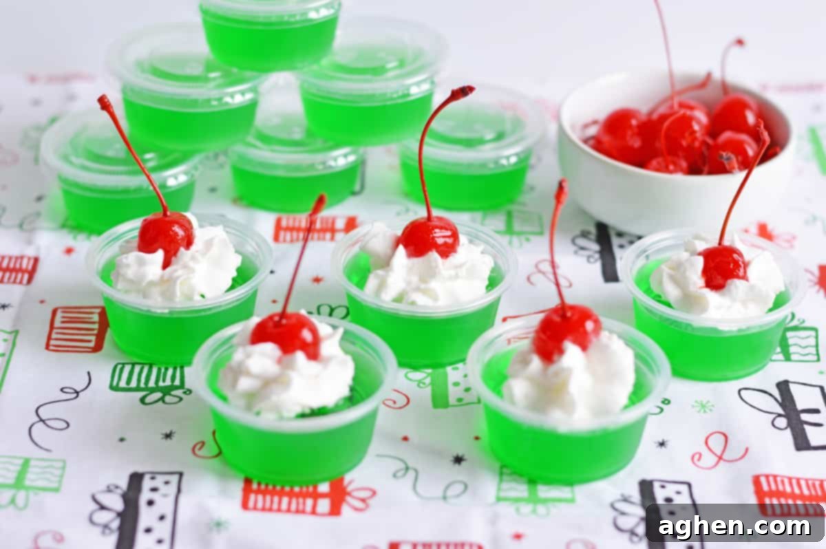 Red and green christmas grinch jello shots topped with whipped cream and cherry