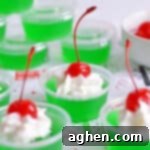 Grinch Jello Shots made with lime jello, tequila, and topped with whipped cream and a maraschino cherry.