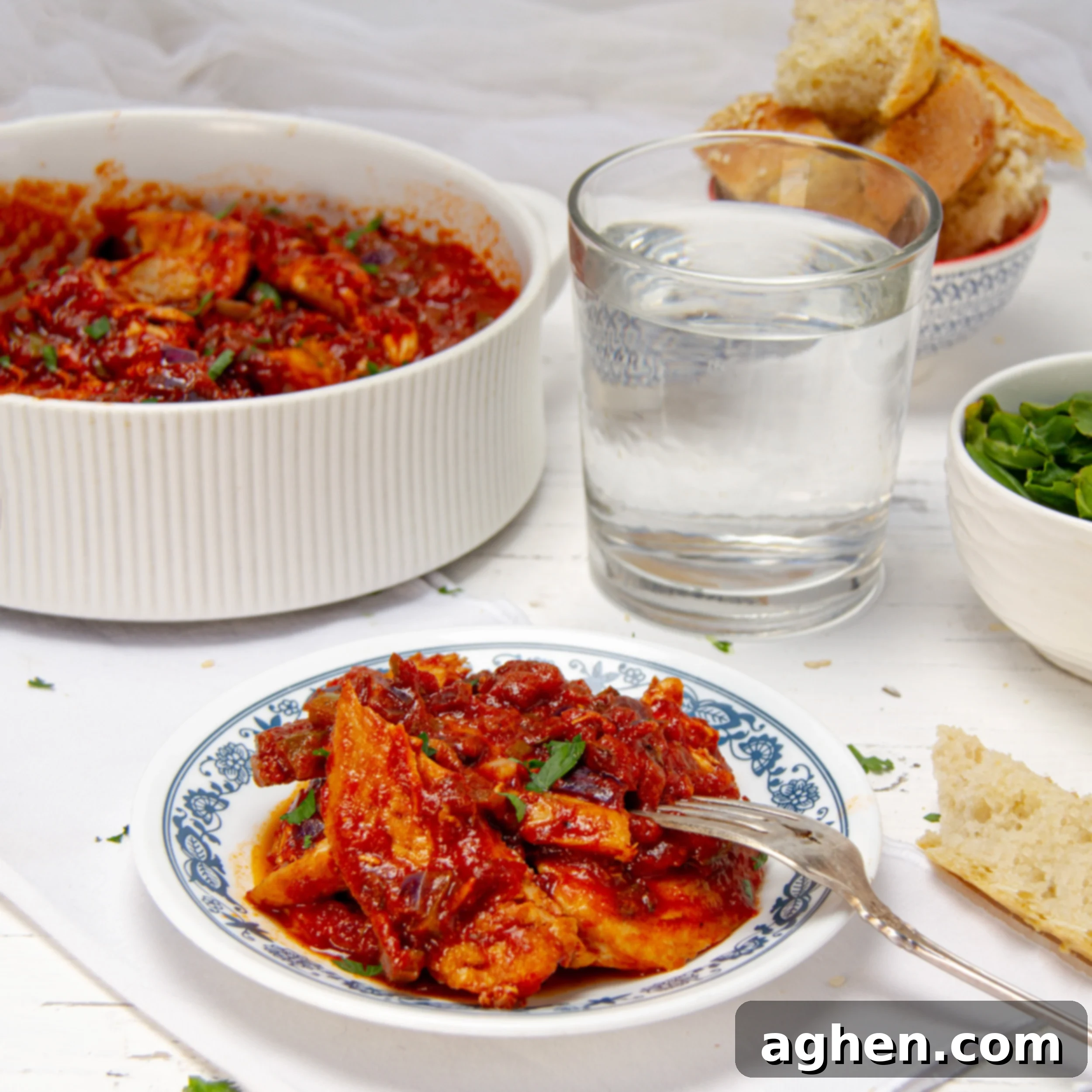 A vibrant plate of New Orleans-inspired Chicken Creole, garnished with fresh parsley and served with a fork. In the background, a large serving platter holds more of the delicious chicken and sauce, ready for sharing.