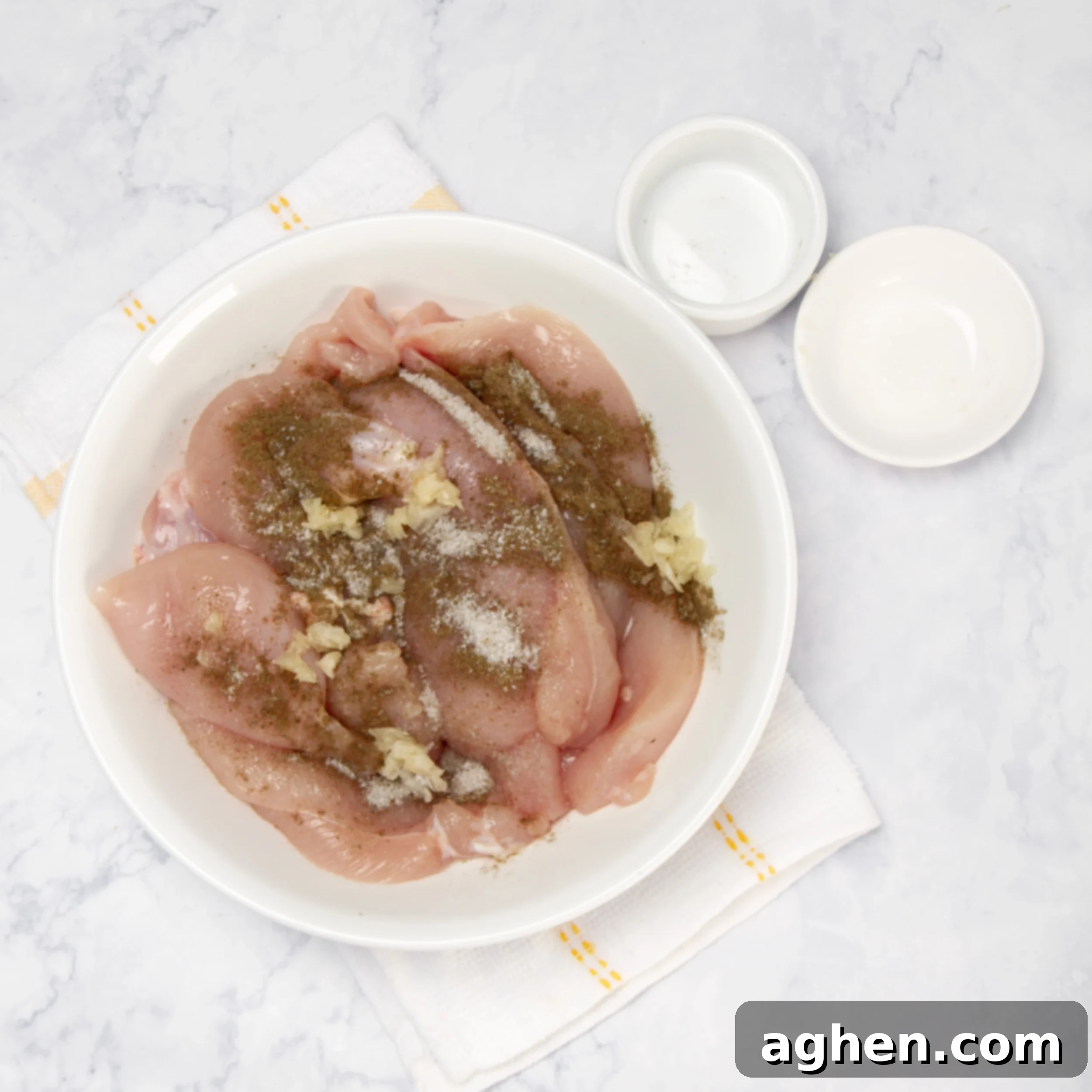Raw chicken breasts generously seasoned with a blend of garlic, cumin, salt, and pepper, resting in a small bowl, ready for marination. The spices are visibly coating the chicken, promising deep flavor.