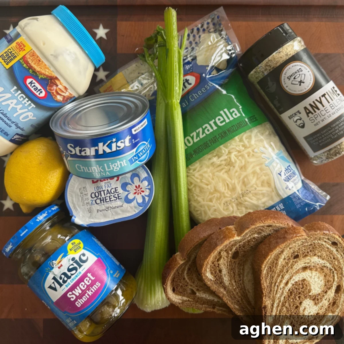 Ingredients laid out for an open-faced tuna melt, including tuna cans, celery, pickles, mayonnaise, lemon, and seasoning.