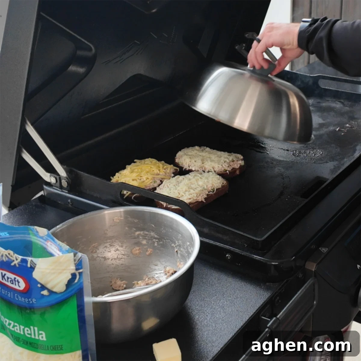 Open-faced tuna melts on a griddle, covered with a hood to melt the cheese.