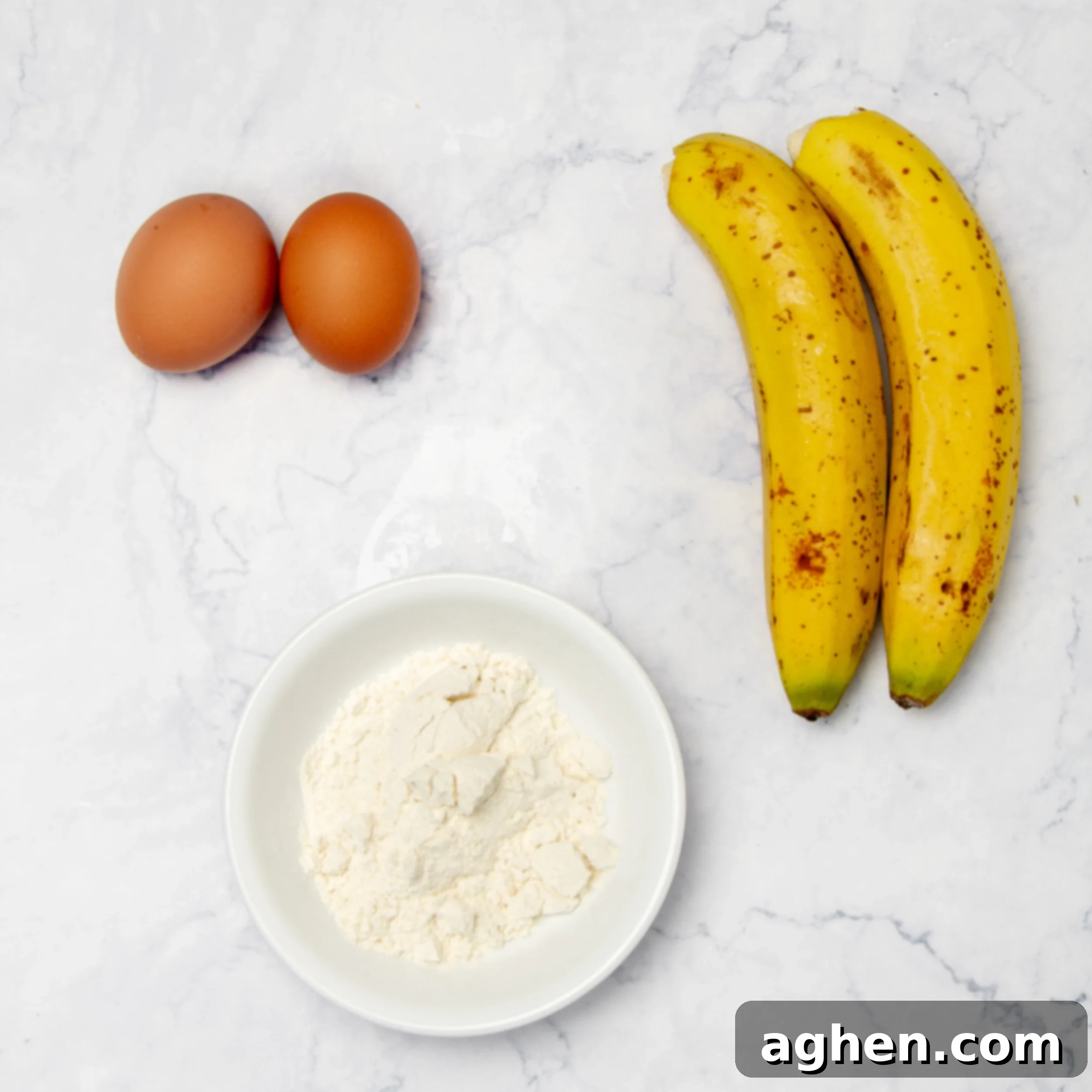 Ingredients of two ripe bananas, two fresh eggs, and a small bowl of all-purpose flour on a kitchen counter.
