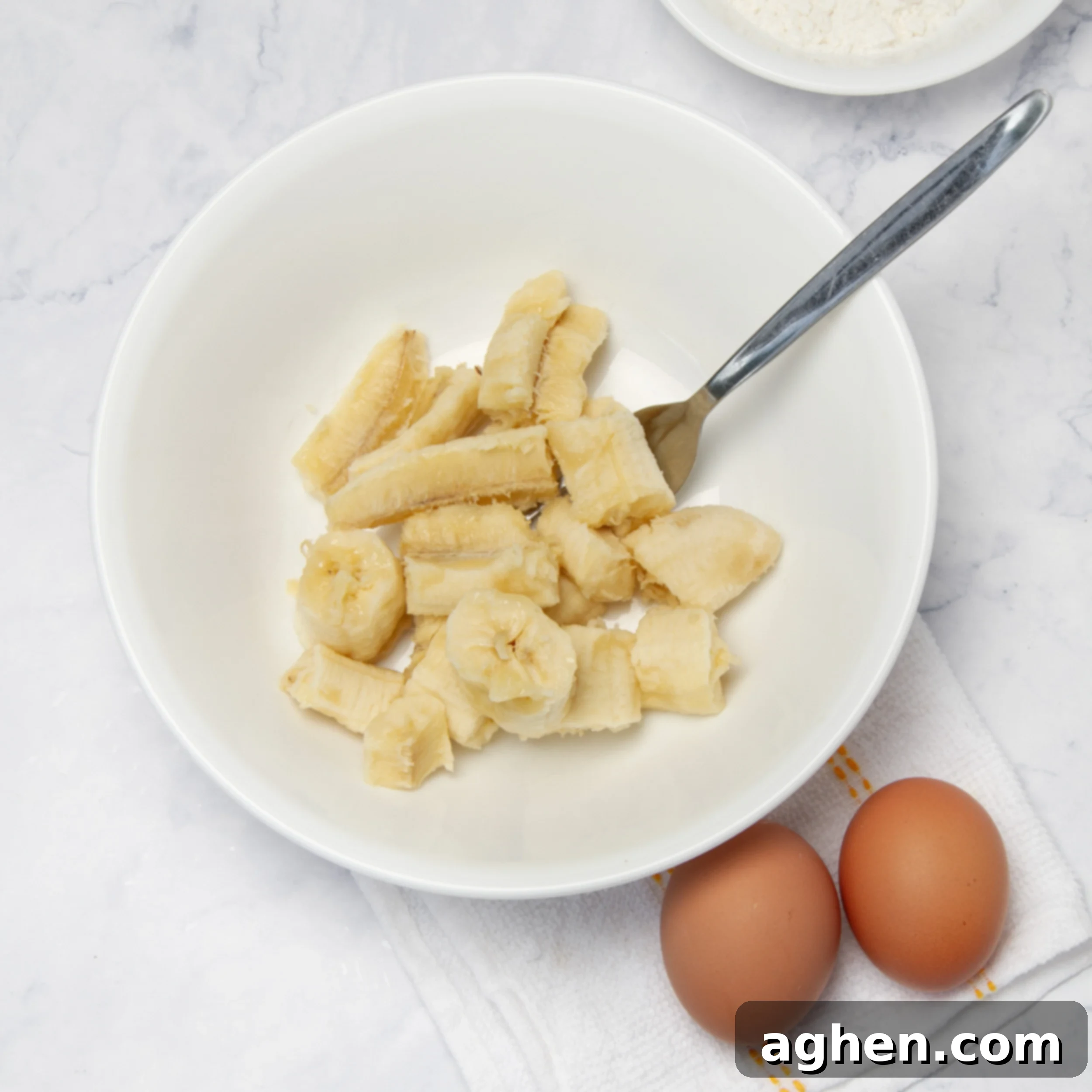 A ripe banana cut into pieces in a small bowl, with two eggs on the side, ready for mashing and mixing.