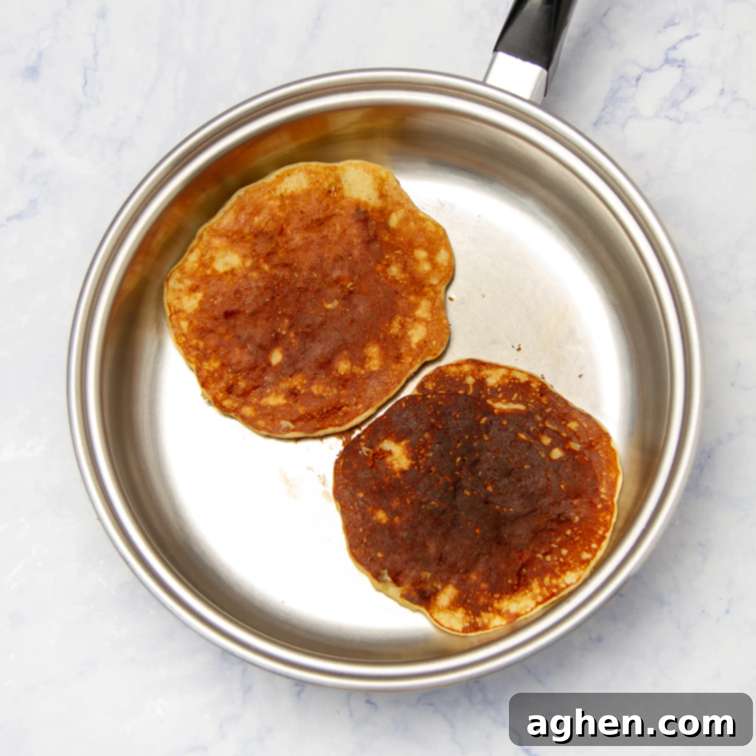 Two banana omelets frying perfectly in a non-stick pan, turning golden brown.