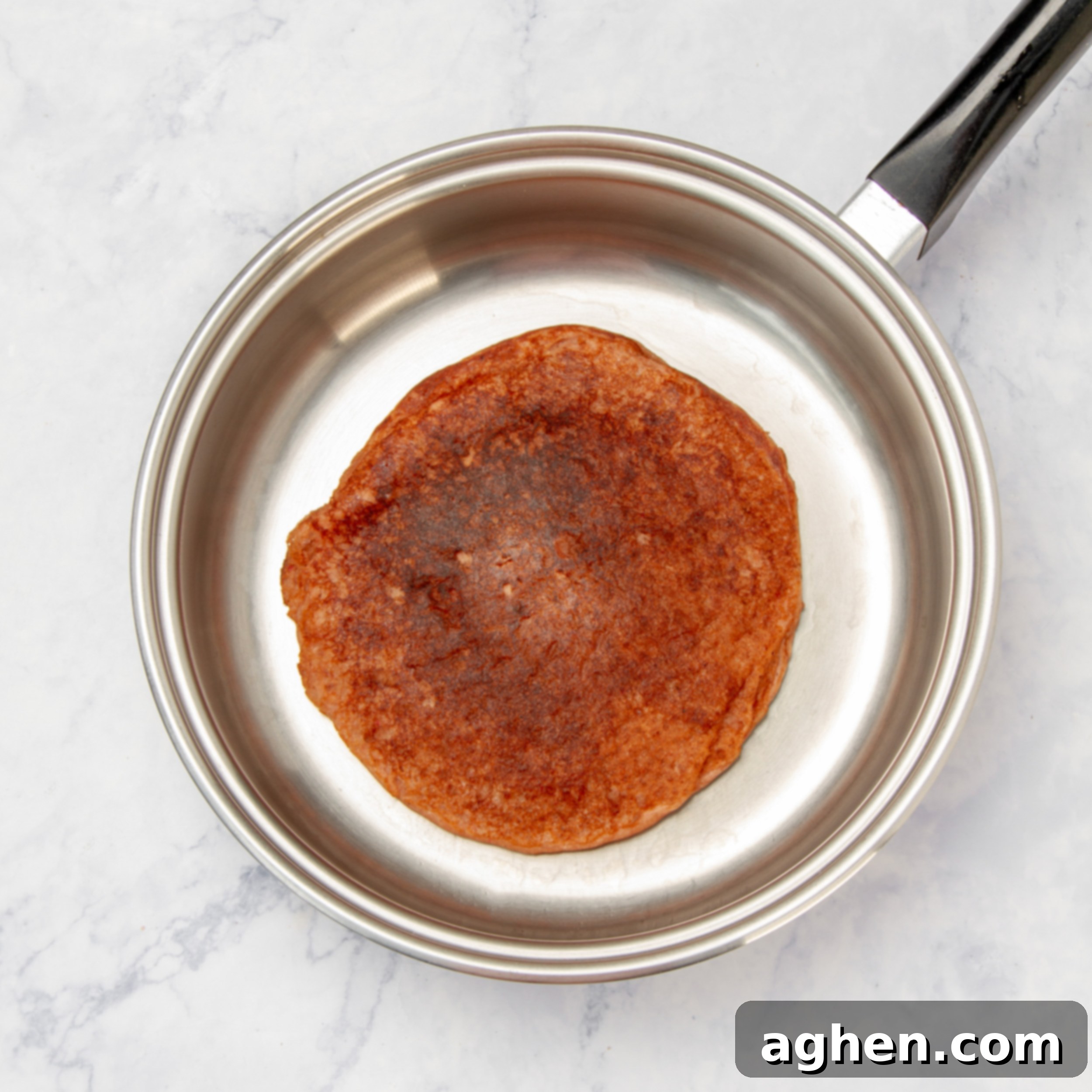 Golden Sweet Potato Pancakes 6 A single sweet potato pancake cooking on a non-stick pan, showing bubbles forming on the surface.