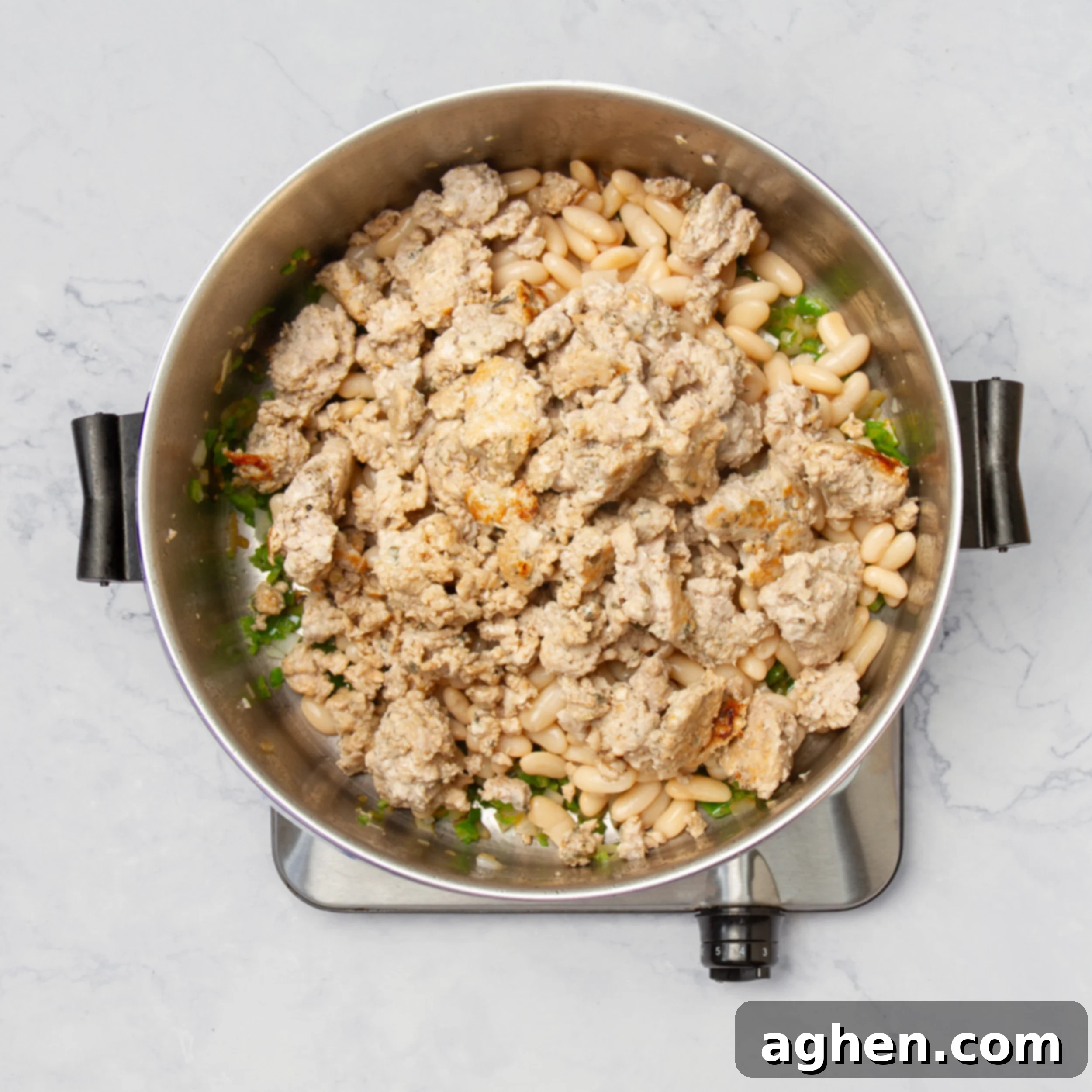 A large pot containing browned ground turkey, sautéed aromatics, and white beans, simmering gently to combine flavors.