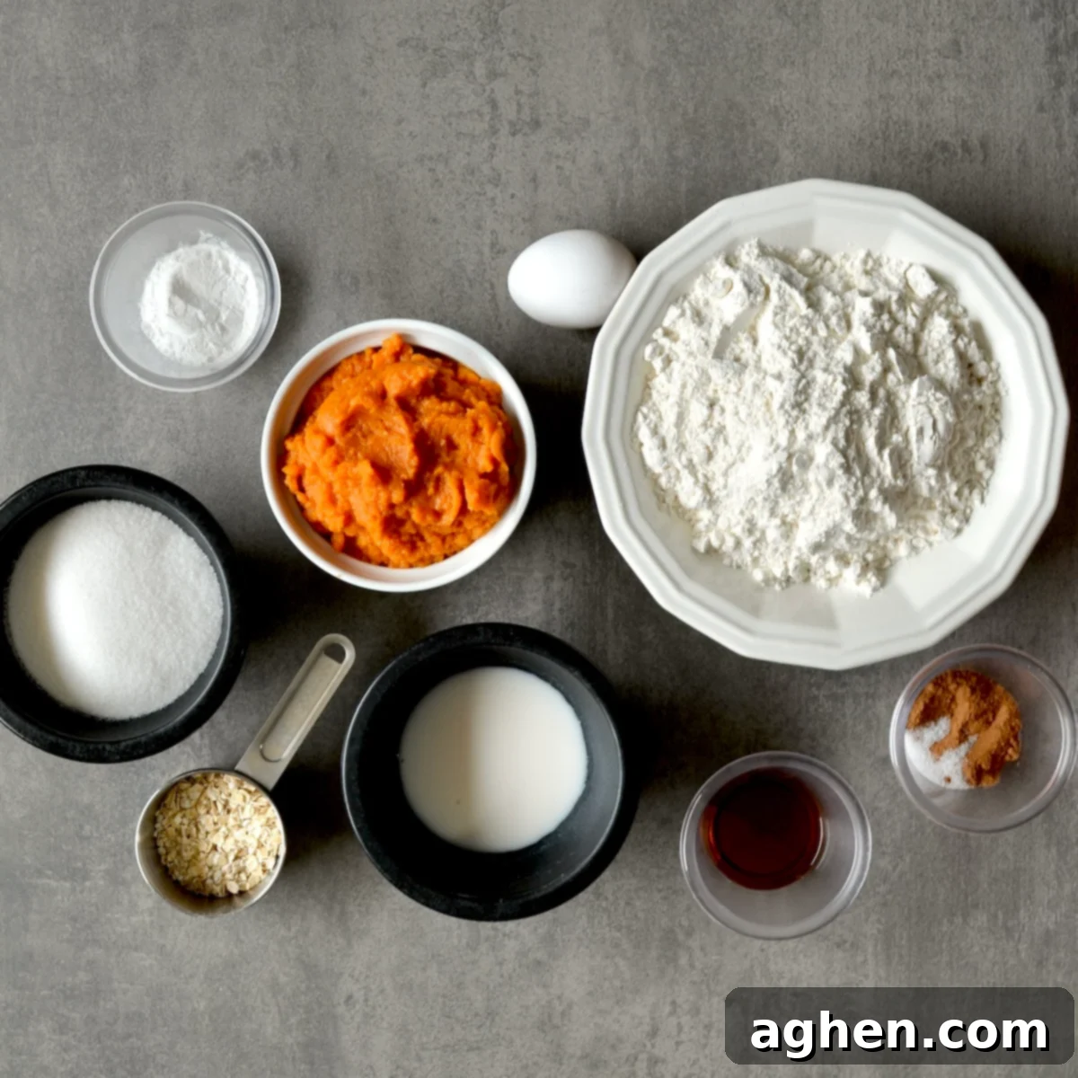 Various ingredients for pumpkin muffins laid out on a table, including flour, spices, pumpkin puree, and milk.