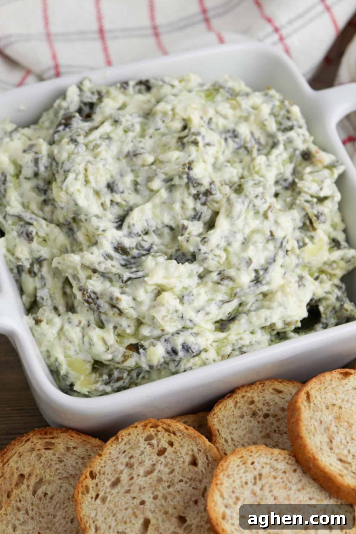creamy crockpot spinach and artichoke dip in white bowl served with small pieces of bread for dipping