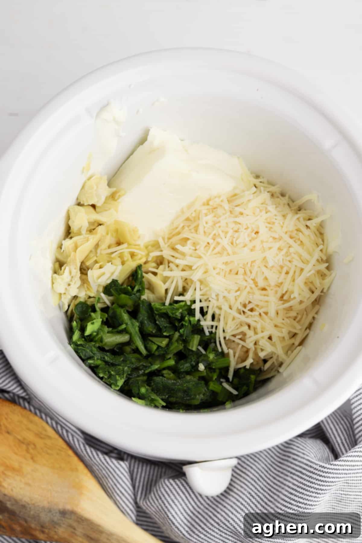 Cream cheese, spinach, artichokes, garlic, and shredded cheese in round white crockpot